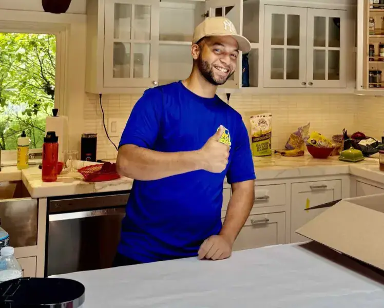 Smiling man in blue shirt gives thumbs-up in kitchen