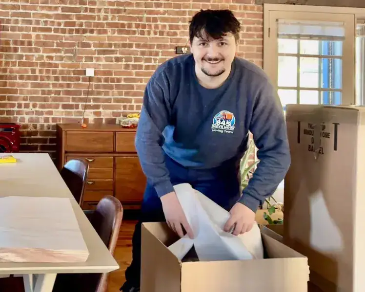 Mover packing items into a cardboard box indoors