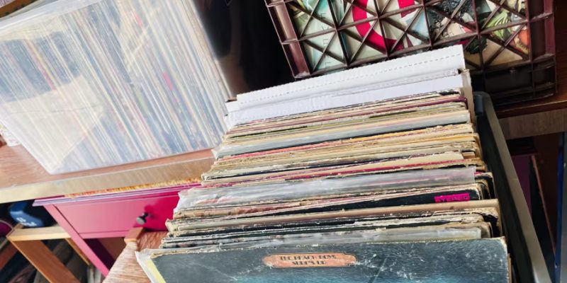 Vinyl records stacked on a shelf, showcasing various album covers, illustrating the careful organization needed for packing records during a move.